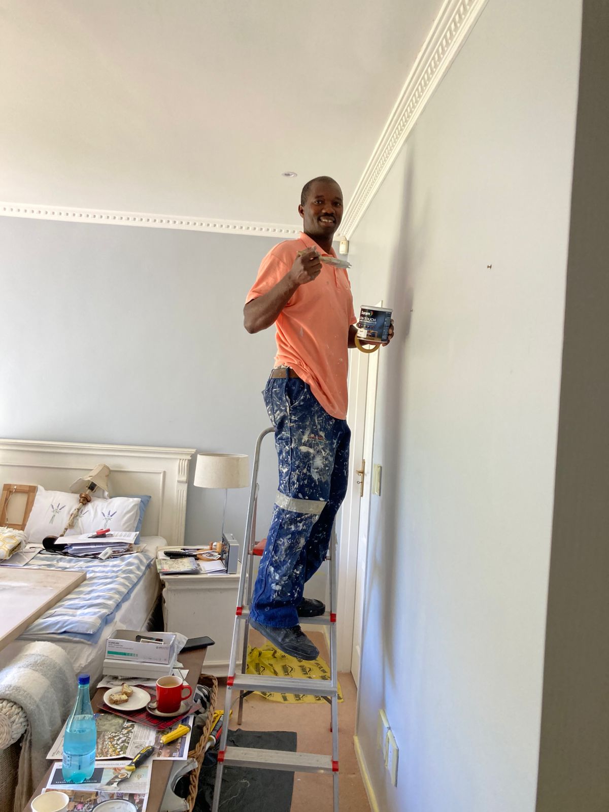 Cryton Chirenda on a step ladder cutting in at a ceiling cornice during an interior repaint