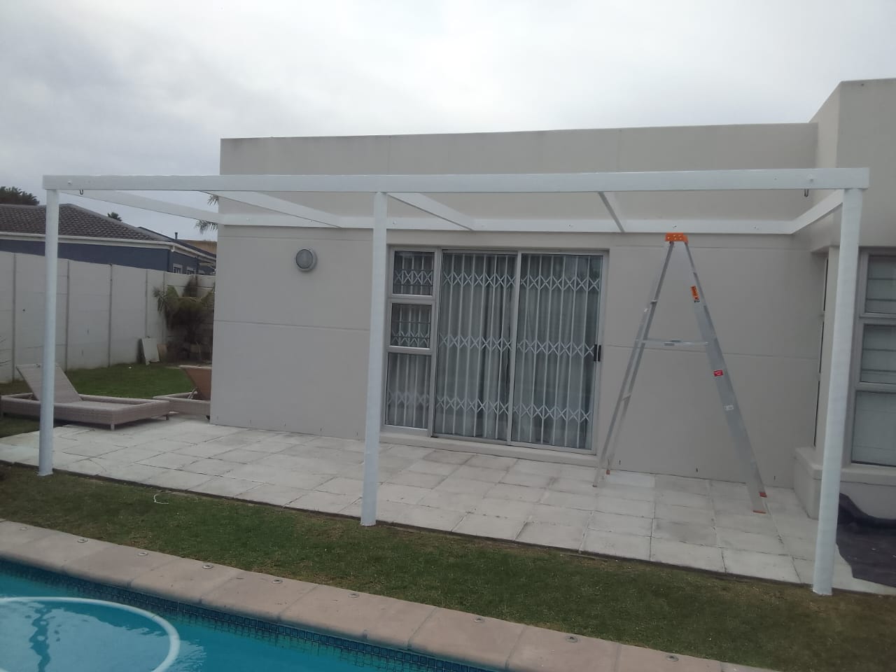 Poolside patio with a freshly painted grey wall and white pergola frame