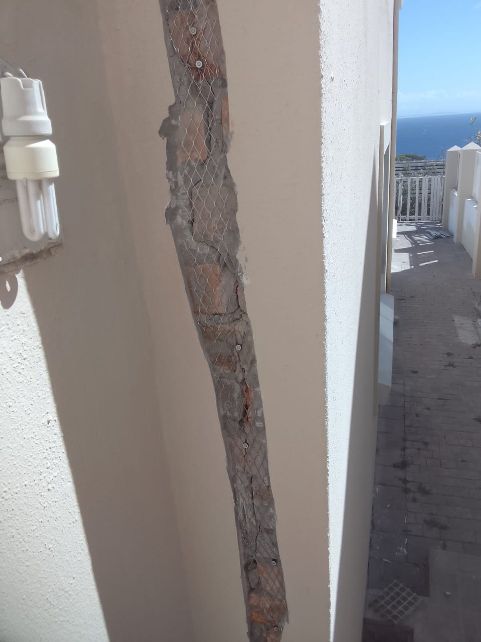 A structural crack raked back to brick with galvanised mesh fixed over it before re-plastering, sea view behind