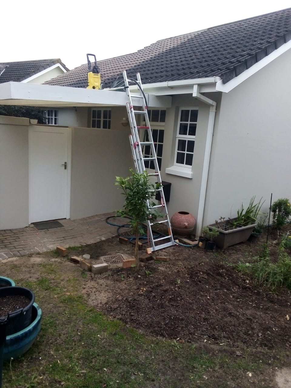 Ladder up to a roof with a pressure washer on the gutter, cleaning down before work