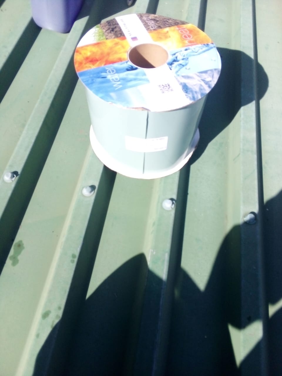 A roll of waterproofing membrane sitting on a green IBR metal roof