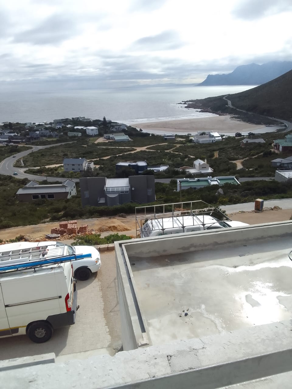 Flat concrete roof being waterproofed with a view over a coastal village and beach