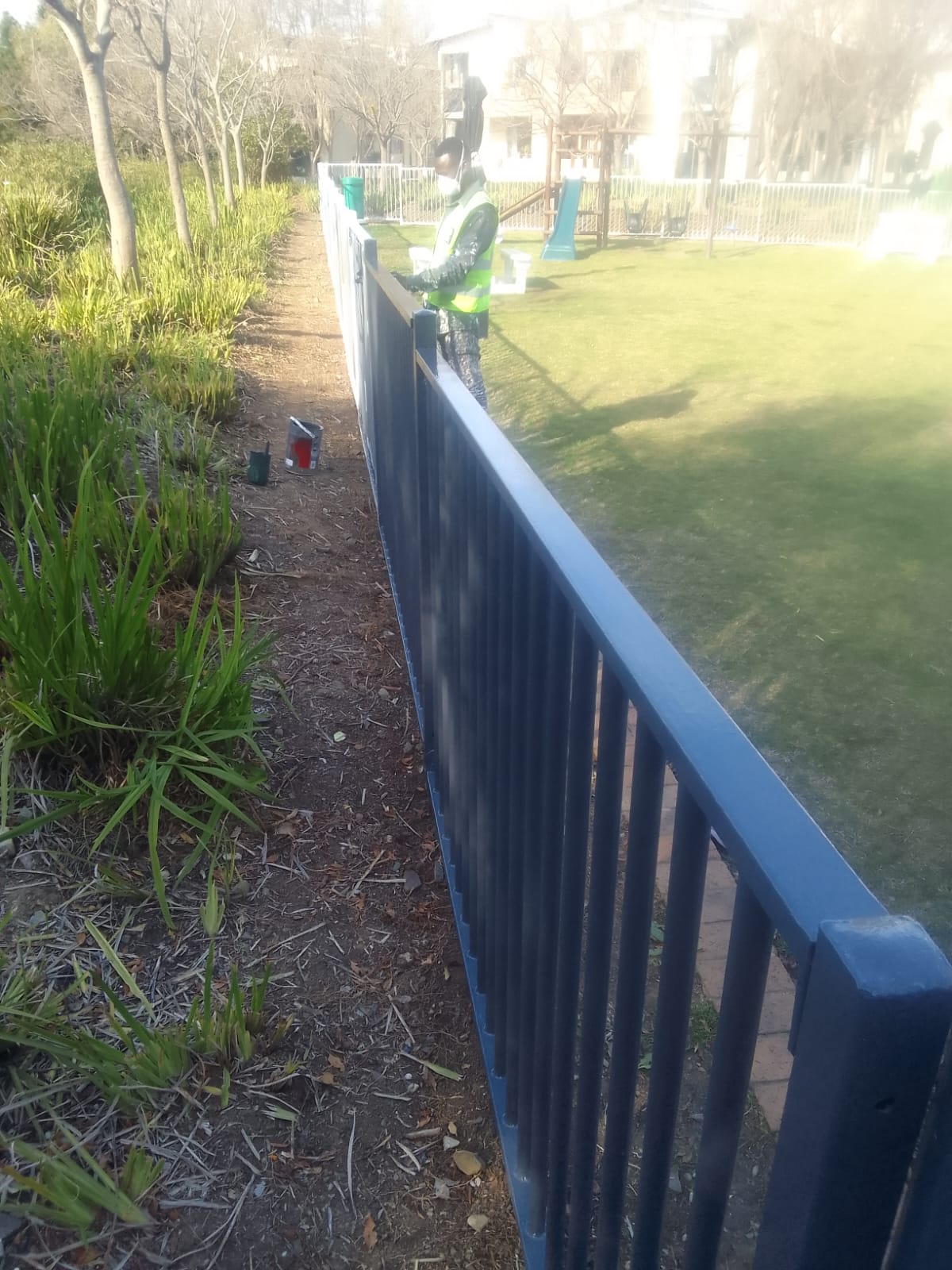 Worker brushing navy enamel onto a complex's boundary railings — a body corporate contract